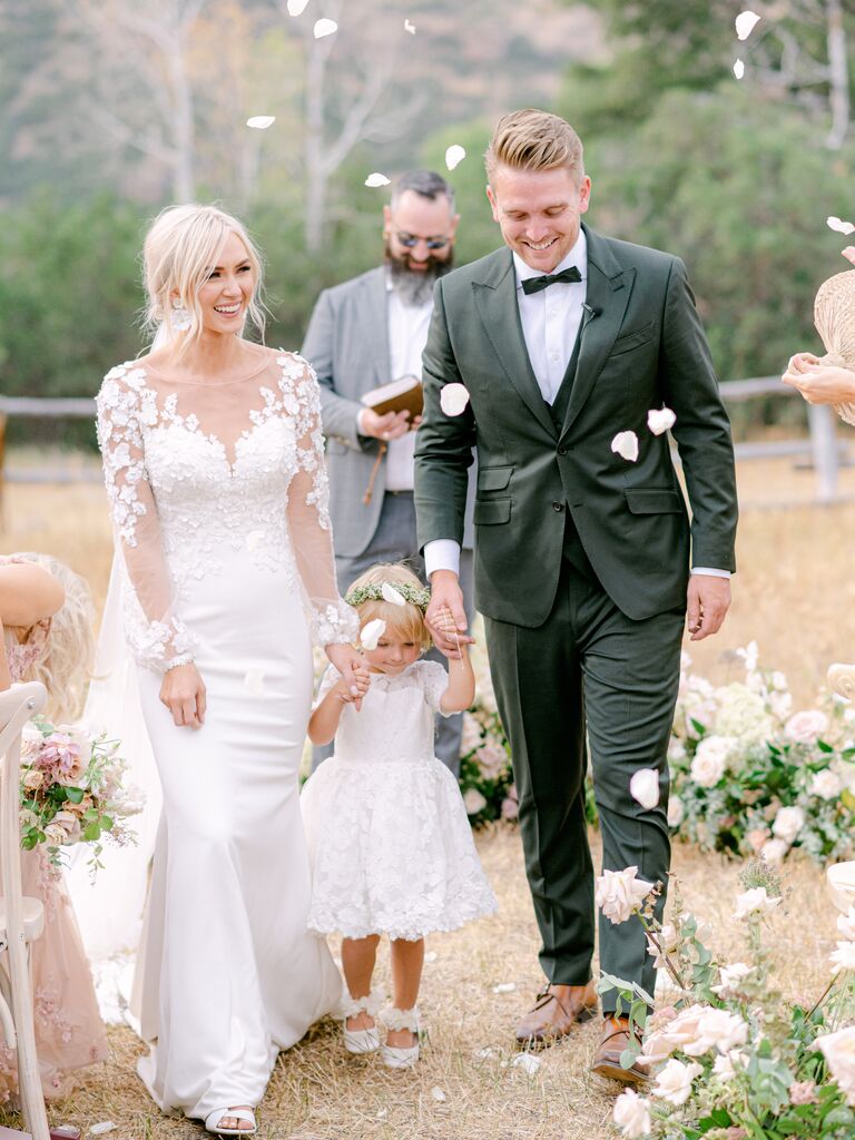 Bride, groom and daughter recess down aisle under rose petals