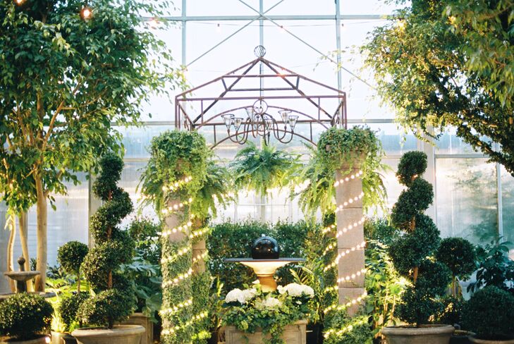 Lauren and Kyle said “I do” in front of this fountain and wedding arch overflowing with greens, illuminated by string lights and a chandelier. This super romantic garden setting influenced their whole wedding style.