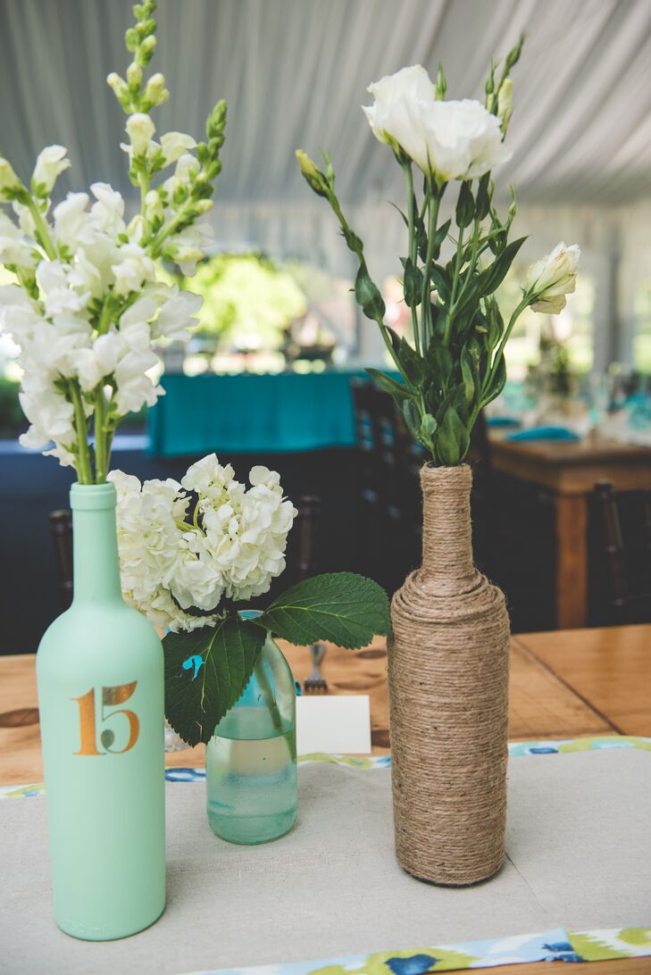 Centerpieces consisted of bottles painted turquoise and wrapped in twine, which were filled with white delphiniums, white roses and white hydrangeas. Some had table numbers stenciled onto them.