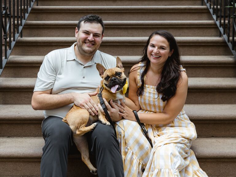To-be-weds with their dog in their lap while sitting on a stoop.