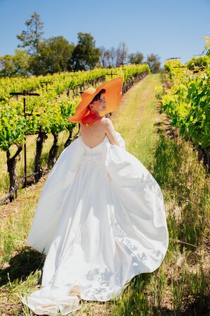 Bride in Strapless Wedding Dress and Oversized Orange Hat in Vineyard