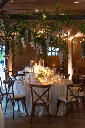 Dimly Lit Barn With Hanging Greenery and Lavender Flowers, Round Tables With Candles