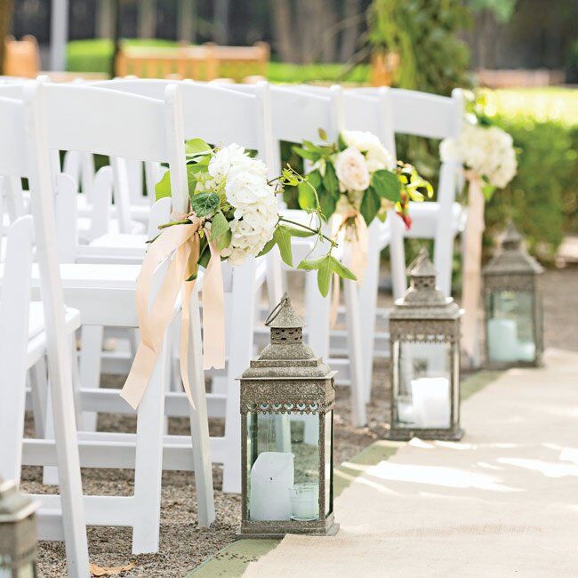 Oversize lanterns lined the ceremony aisle by white wooden folding chairs and clusters of white hydrangeas.