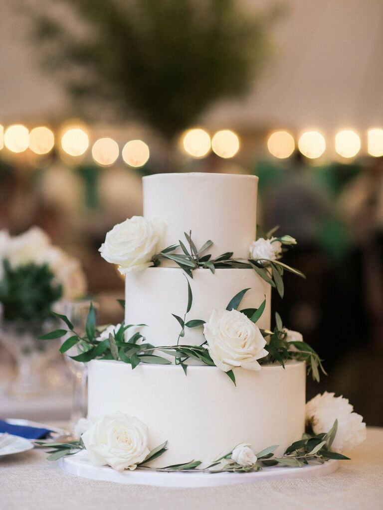 three tier white wedding cake decorated with greenery and white roses