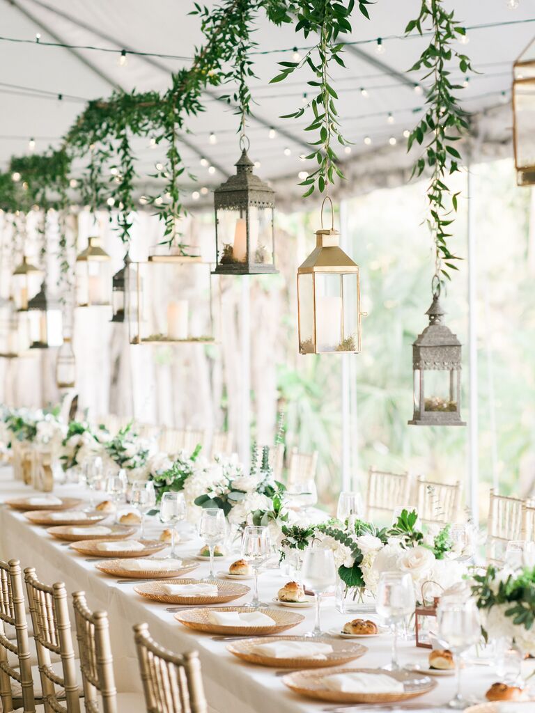 long wedding reception table with greenery garland and mismatched silver and gold lanterns hanging above