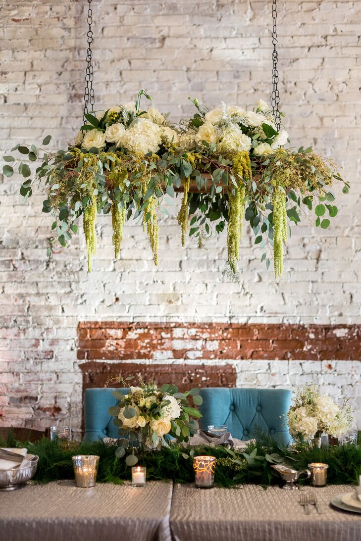 Wedding planner Martha Stilwell, from Details by Martha, worked her magic at the reception. She accented the head table with a textured champagne linen and a lush table runner. Wooden swings were suspended from the ceiling above the table. They were topped with hanging amaranthus, eucalyptus, hydrangeas, roses and hypericum.