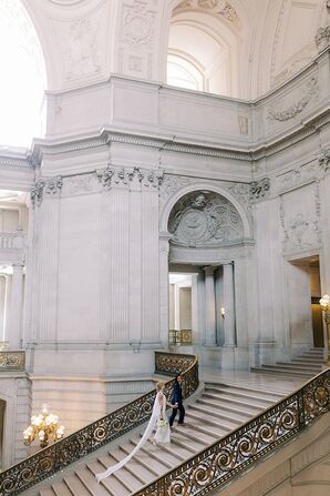 Couple in Dark Suit and Dress With Long Train Walking Up San Francisco City Hall Steps