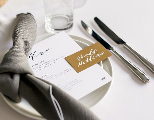 modern wedding reception place setting with gray tied napkin and gold place card with white calligraphy