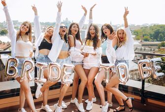group of bridesmaids and bride posing next to bride to be balloons wearing matching outfits