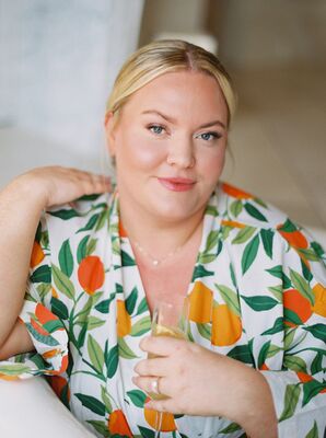 Bride in Robe With Oranges, Greenery Holding Champagne With Light Makeup