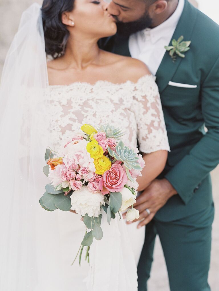bride kisses groom as she holds posy wedding bouquet of ranunculus, succulents, roses and eucalyptus