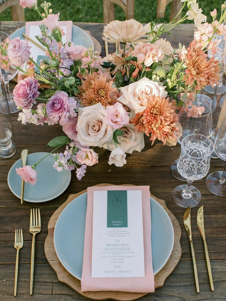 A beautiful table setting sits beneath a riotous floral arrangement in shades of peach and pink.