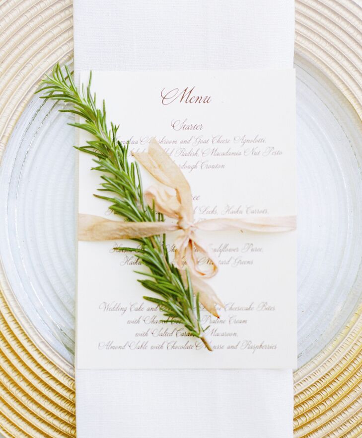 A sophisticated menu card tied up with a sprig of rosemary sat atop gold chargers for a simple, yet elegant place setting.