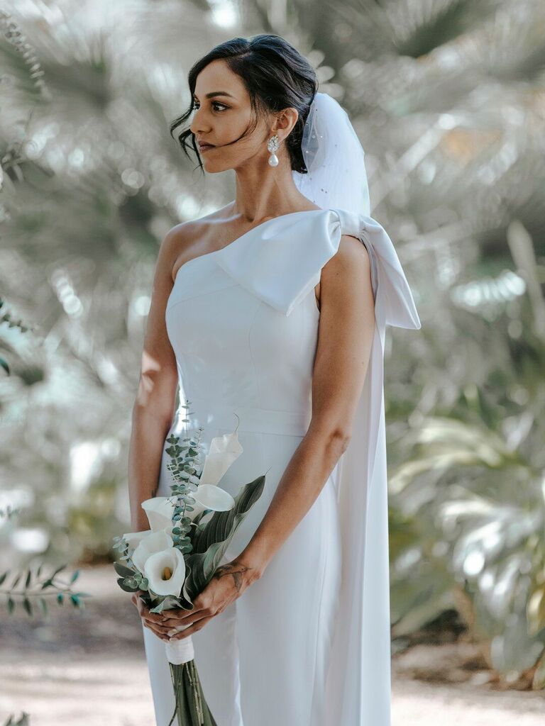 bride wearing minimalist white wedding jumpsuit with oversized bow on one shoulder