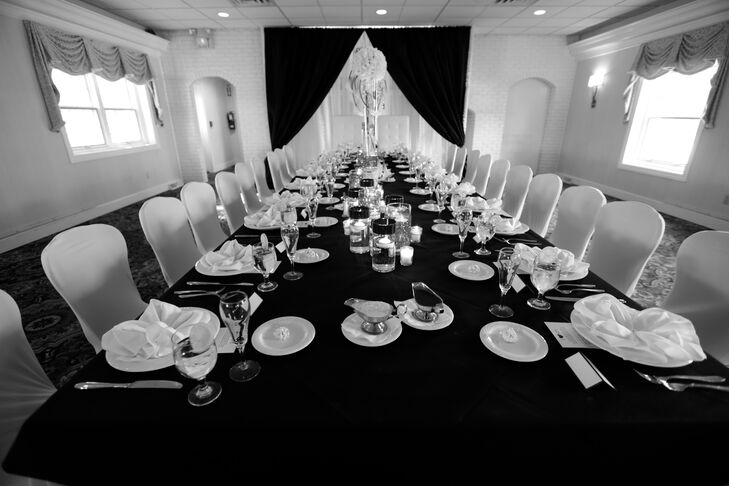 The long head table at the wedding reception was dressed in a lack tablecloth and had white dinnerware set.