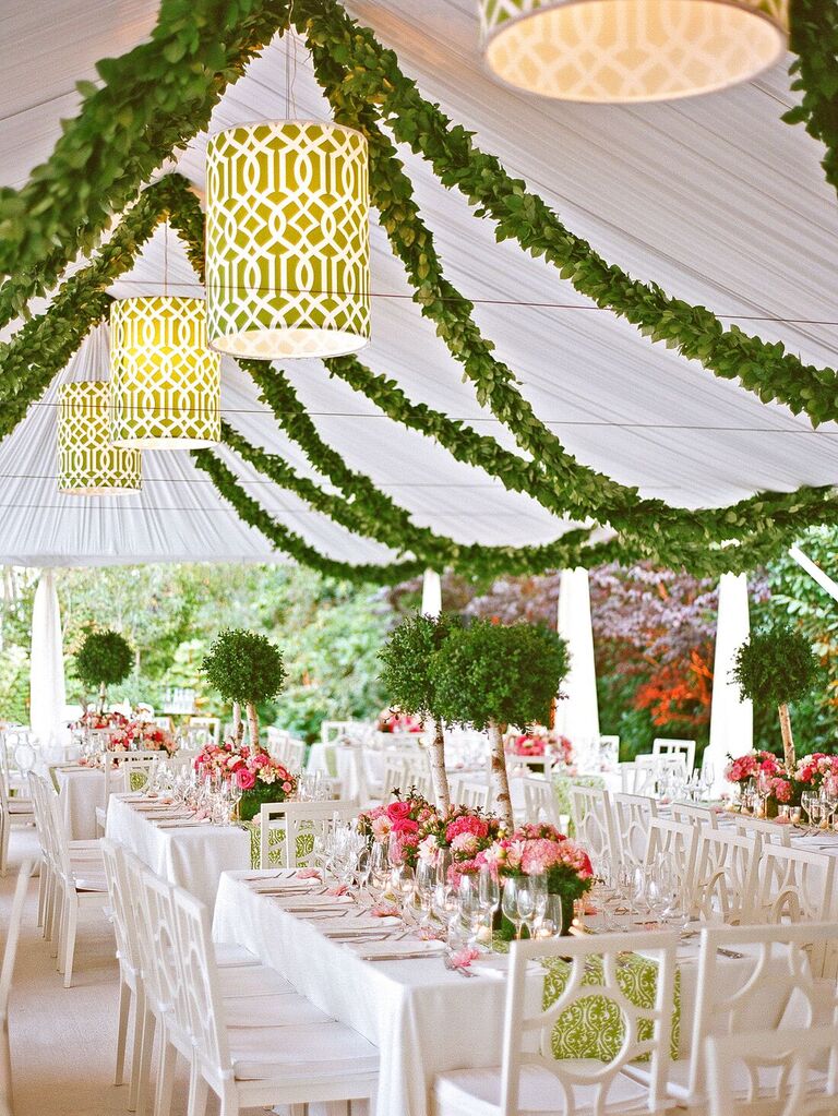preppy indoor wedding reception decor with greenery garlands and green patterned lampshades hanging from white cloth tent ceiling