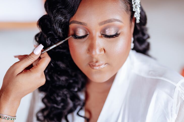 A bride gets her glamorous wedding hair and makeup done, complete with blush pink eye shadow with shimmer, big lashes, a wavy down hairstyle and an elegant crystal hair clip.