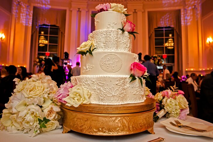 The timeless four-tiered white buttercream cake was decorated with lace pipping to complement the brides wedding gown and topped with fresh flowers.
