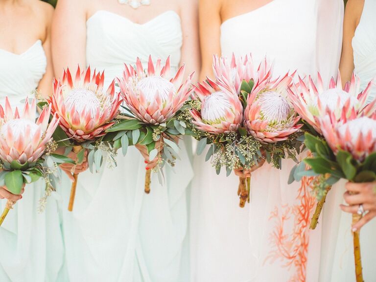 A bride and her wedding party hold vibrant protea bouquets.