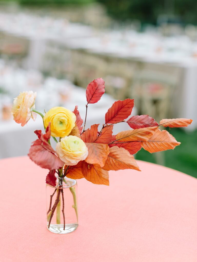 fall wedding centerpiece with orange and red leaves and yellow ranunculus