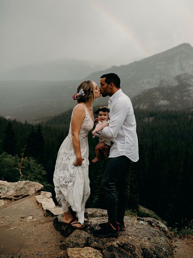 couple kissing on top of mountain and holding baby