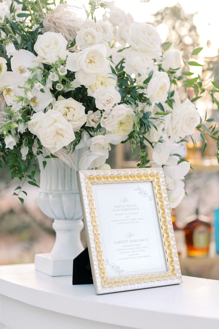 Floral Arrangement With White Orchids and Roses Beside Framed Sign