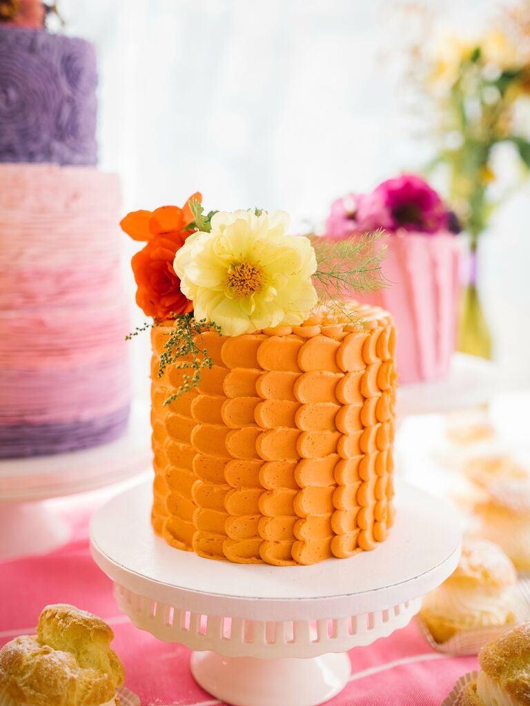 A summery orange buttercream wedding cake topped by fresh flowers.