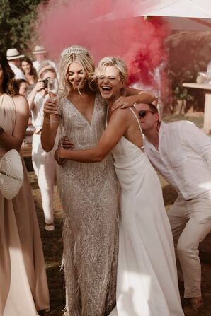 Bride in Beaded Gown With Tassels, Crown, and Bride in Sleek Gown Embrace, Pink Smoke