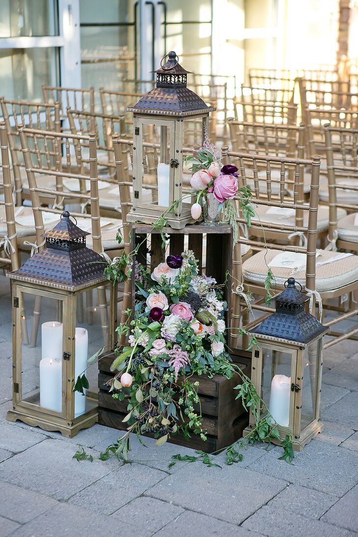 Arrangements of wooden lanterns with candles and wooden crates overflowing with greens, white, pink and blush roses marked the entryway to the ceremony at Stone House at Stirling Ridge in Warren, New Jersey.