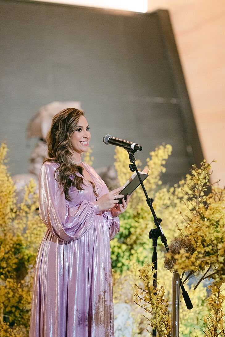 Woman in Shimmering Purple Gown Speaking at Modern Ceremony, Yellow Flowers