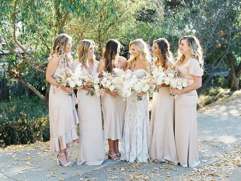 A bride and her wedding party pose for a photo in neutral tones.