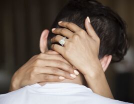 couple embracing with woman's hands with engagement ring behind man's neck
