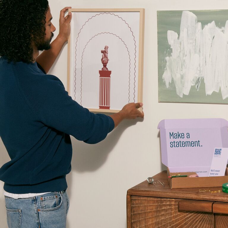 Man creating gallery wall with framed art work and Character tools