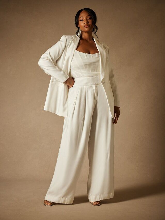 Model wears billowy white trousers with a fitted top and matching blazer. 