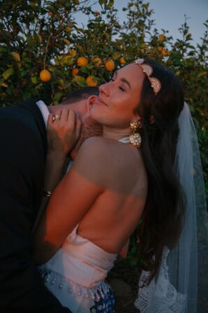 Groom Embraces Bride in Gold Headpiece, Gold Statement Earrings, Low-Back Outfit at Sundown