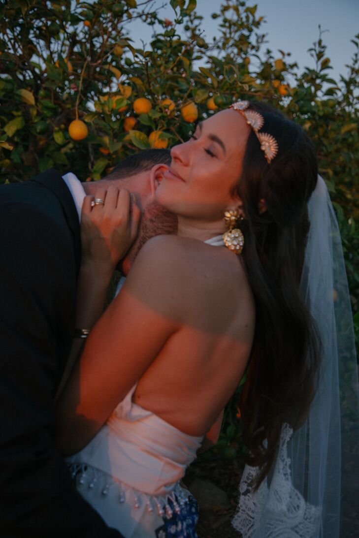 Groom Embraces Bride in Gold Headpiece, Gold Statement Earrings, Low-Back Outfit at Sundown