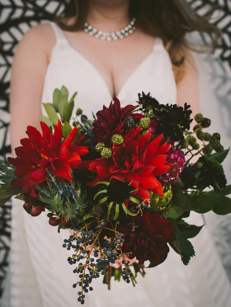 Bride holds a wintery bouquet of red dahlias and greenery. 