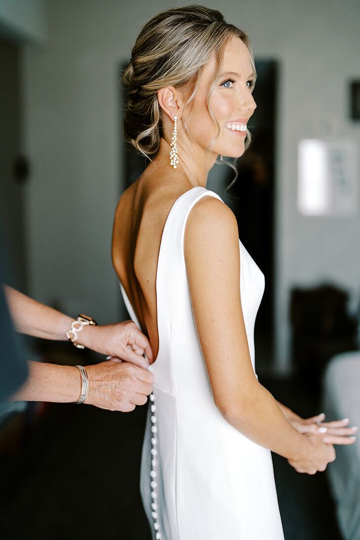 Bride Getting Into Dress With Light Makeup, Dangling Earrings and an Updo
