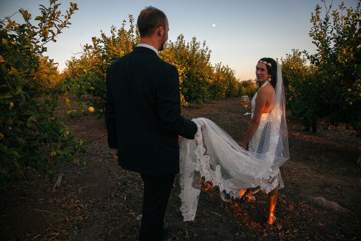 Groom Holding Bride's Long Lace Veil As They Walk Through Lemon Tree Grove, Multi-Piece Dress
