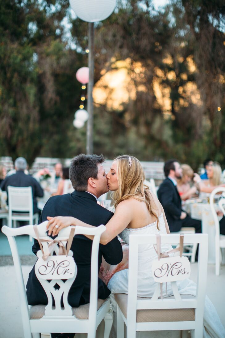 Monique and Shade sat in white antique chairs at the sweetheart table, draped with white wooden "Mr." and "Mrs." signs hanging by champagne-colored ribbon.