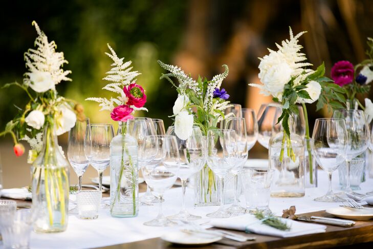 Reception tables were decorated with white hemstitch table runners and floral arrangements of ranunculus and astilbe in mixed vintage glass vessels created a lush, wildflower look.