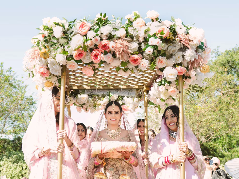 A bride walks beneath a canopy of pink flowers.