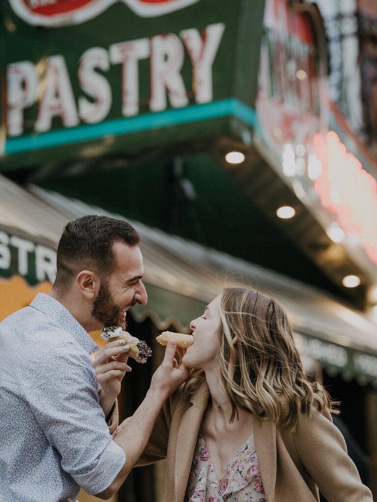 Couple feeds each other cannolis outside their favorite pastry shop. 