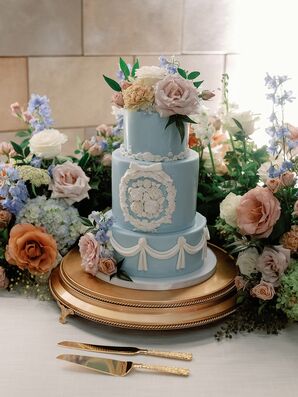 Three-Tier Pale Blue Cake With Ornate White Designs and Details, Fresh Flowers on Gold Stand