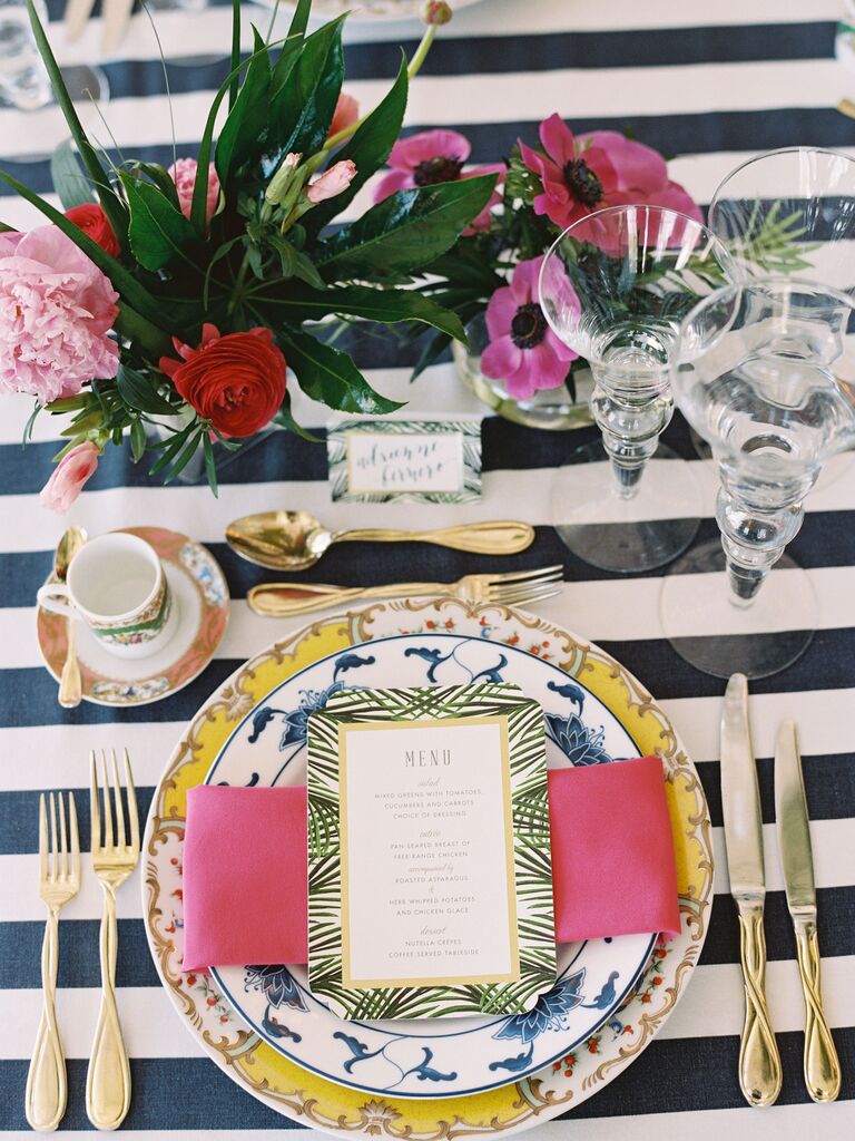 Place setting with gold flatware, striped linens and tropical centerpieces
