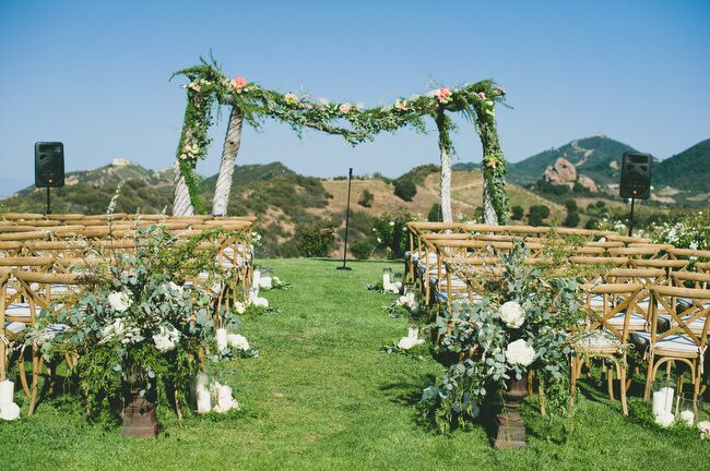 The ceremony was held at Saddlerock Ranch’s Chateau Le Dome site, overlooking the rolling hills of Malibu, California, and the Santa Monica Mountains in the distance. To match the Tuscan-like setting, the couple lined the aisles with rustic country chairs, hurricane vases filled with white pillar candles and arrangements of eucalyptus and white peonies.