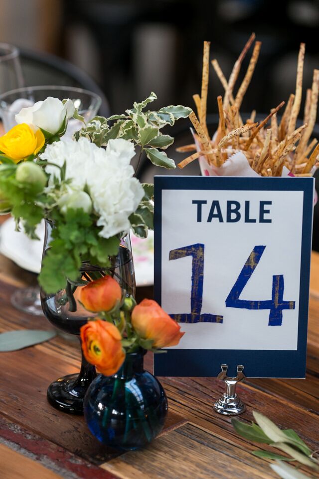 White, green and orange floral centerpieces in colorful glass bottles and vases decorated long farm tables at Ovation Chicago in Chicago, Illinois.