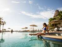 a woman sitting on the edge of a pool splashing her feet and laughing in cabo san lucas mexico