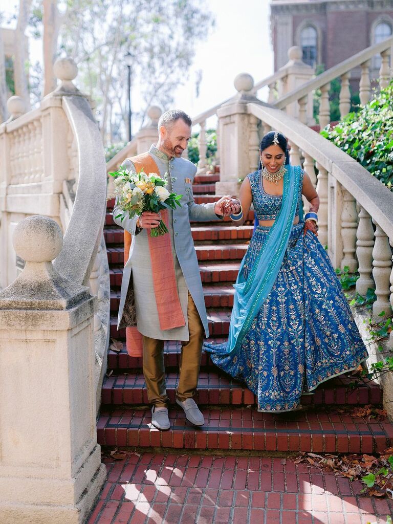 bride and groom walk down the steps wearing south asian wedding attire