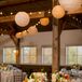 Wooden farm tables with neutral table runners and brown chiavari chairs added to the rustic ambience inside barn reception at the Mountain Top Inn & Resort in Chittenden, Vermont. Low centerpieces of ivory and orange flowers continued the fall theme, and paper lanterns and string lights overhead brought out a romantic ambience.